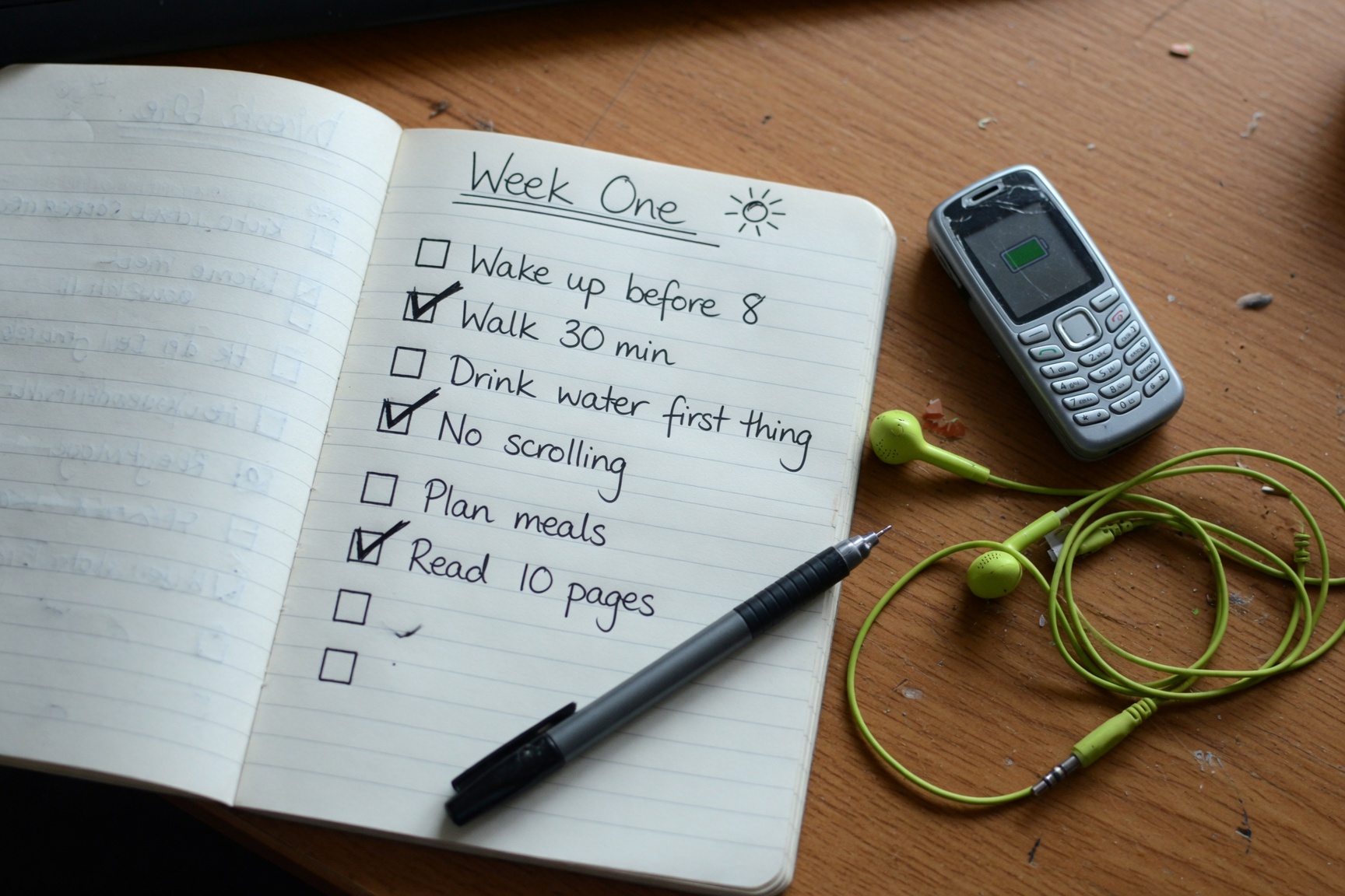 Open notebook with week-one dumbphone habit checklist and earbuds beside a simple phone